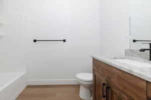 Full bath with vanity, wood finished floors, toilet, baseboards, and a bathing tub