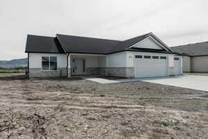 Ranch-style home featuring an attached garage, roof with shingles, stone siding, and concrete driveway