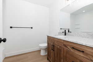 Bathroom featuring toilet, baseboards, wood finished floors, and vanity