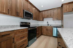 Kitchen with stainless steel appliances, brown cabinetry, a sink, and light wood-style floors