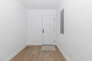 Doorway with baseboards, electric panel, and light wood-type flooring