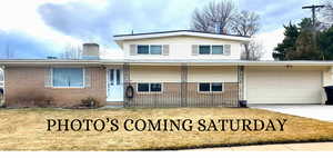 Split level home with driveway, brick siding, a chimney, and an attached garage