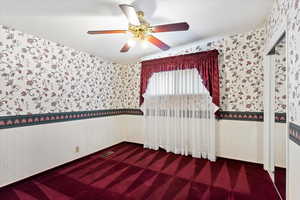 Unfurnished room with visible vents, a wainscoted wall, a ceiling fan, carpet, and wallpapered walls