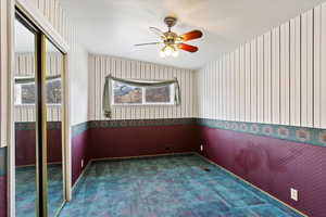 Carpeted empty room with wallpapered walls, baseboards, and ceiling fan