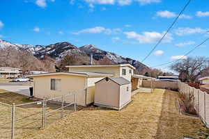 Rear view of house with a gate, an outdoor structure, a storage shed, a lawn, and a mountain view