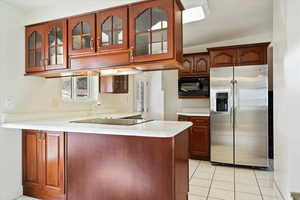 Kitchen featuring glass insert cabinets, black appliances, a peninsula, and light countertops