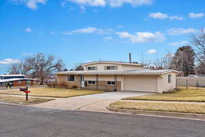 Tri-level home with brick siding, a front lawn, fence, concrete driveway, and an attached garage