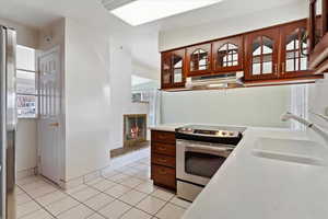 Kitchen featuring under cabinet range hood, light countertops, light tile patterned floors, appliances with stainless steel finishes, and a sink