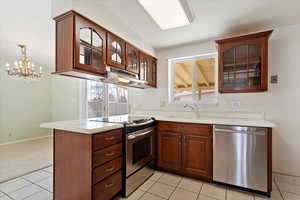 Kitchen with under cabinet range hood, a sink, appliances with stainless steel finishes, a peninsula, and light countertops