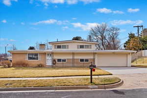 Split level home featuring concrete driveway, a front yard, a garage, brick siding, and a chimney