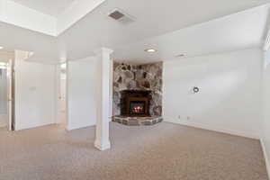 Unfurnished living room with visible vents, baseboards, a stone fireplace, and carpet flooring