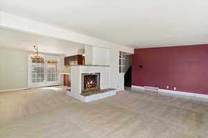 Unfurnished living room featuring an inviting chandelier, a fireplace, visible vents, and light carpet