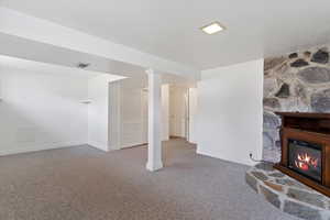 Basement featuring a stone fireplace, carpet, visible vents, and baseboards