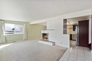 Unfurnished living room with light carpet, light tile patterned floors, a brick fireplace, and baseboards