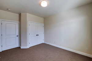 Unfurnished bedroom with baseboards, dark colored carpet, and a closet