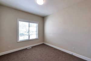 Spare room featuring baseboards, visible vents, and dark colored carpet