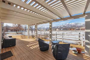 Snow covered deck with a mountain view, fence, and a pergola