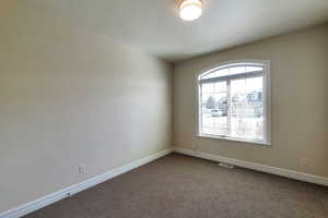 Empty room featuring visible vents, baseboards, and dark colored carpet