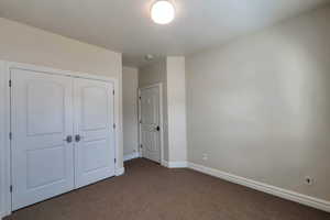 Unfurnished bedroom with a closet, baseboards, and dark carpet