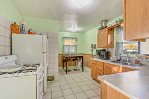 Kitchen with white gas stove, light tile patterned flooring, a sink, light countertops, and wainscoting