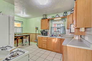 Kitchen featuring white appliances, a wainscoted wall, a sink, light countertops, and a textured ceiling