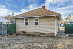 Rear view of property with fence, roof with shingles, and a chimney