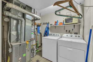 Laundry area featuring laundry area, light tile patterned floors, water heater, and washer and clothes dryer