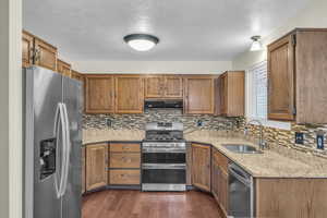 Kitchen featuring under cabinet range hood, brown cabinets, appliances with stainless steel finishes, dark wood-style floors, and a sink