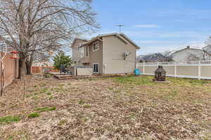 Back of house with a hot tub, an outdoor fire pit, a wooden deck, a lawn, and a fenced backyard