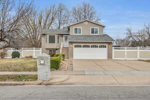 View of front of property featuring brick siding, driveway, a garage, and fence