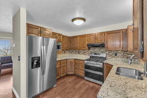 Kitchen with brown cabinets, under cabinet range hood, a sink, dark wood finished floors, and appliances with stainless steel finishes