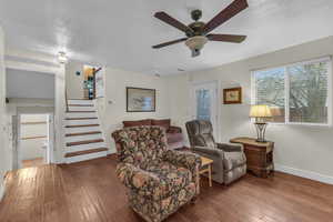 Living area with stairway, baseboards, a ceiling fan, and wood-type flooring