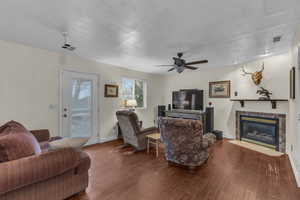 Living area with visible vents, a ceiling fan, wood finished floors, a glass covered fireplace, and baseboards