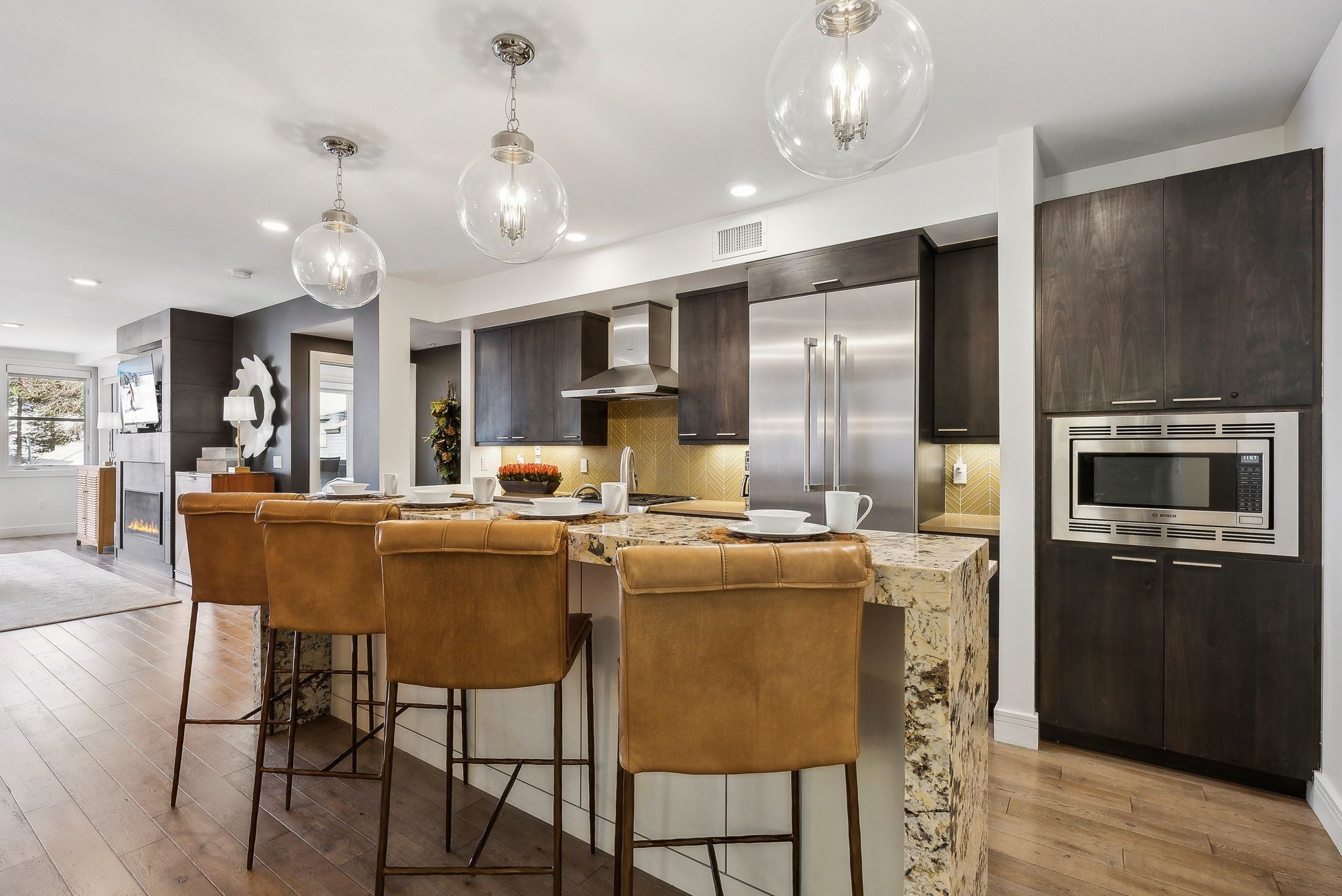 Kitchen with dark brown cabinetry, light wood-style floors, built in appliances, wall chimney range hood, and tasteful backsplash
