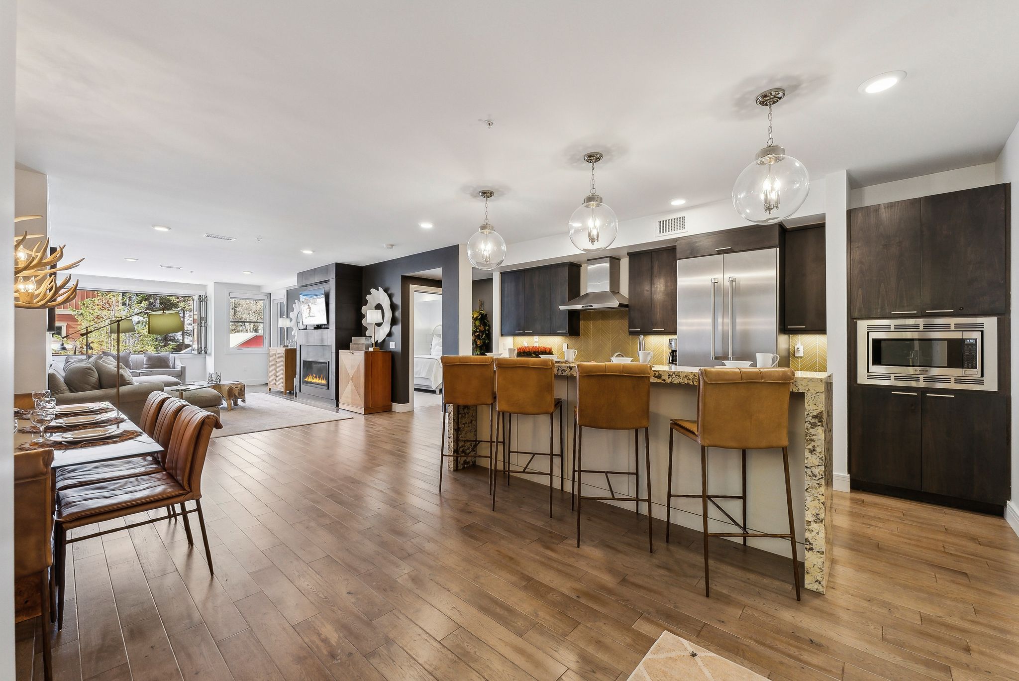Kitchen with a kitchen bar, light wood finished floors, wall chimney exhaust hood, light countertops, and built in appliances