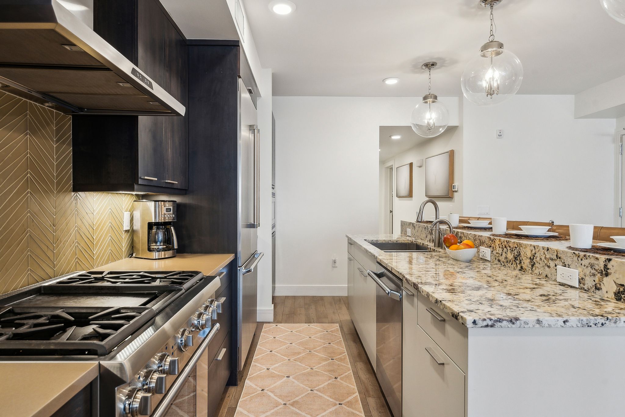 Kitchen featuring a sink, decorative light fixtures, backsplash, appliances with stainless steel finishes, and wall chimney exhaust hood