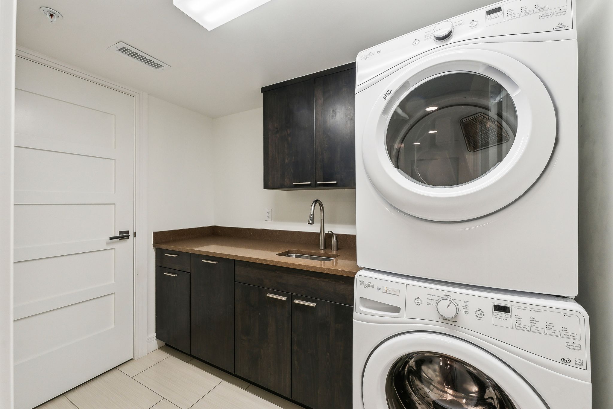 Laundry area featuring visible vents, stacked washer and dryer, a sink, cabinet space, and light tile patterned floors