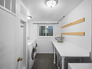 Clothes washing area with clothes dryer, cabinet space, a textured ceiling, and dark tile patterned flooring