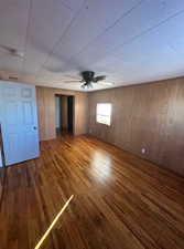 Unfurnished bedroom with wood walls, dark wood-type flooring, and ceiling fan