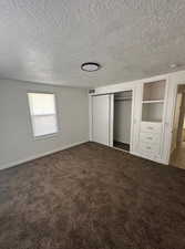 Unfurnished bedroom featuring dark colored carpet, a closet, and a textured ceiling