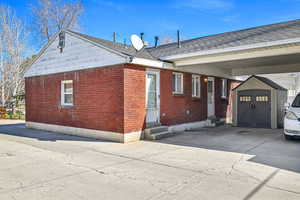 Exterior space featuring brick siding, entry steps, an outbuilding, driveway, and a storage unit