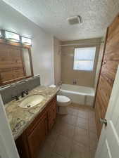 Bathroom with vanity, bathtub / shower combination, light tile patterned floors, and a textured ceiling