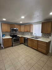 Kitchen with light countertops, appliances with stainless steel finishes, light tile patterned floors, brown cabinetry, and a textured ceiling