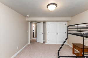 Bedroom with light colored carpet, baseboards, a closet, and a textured ceiling