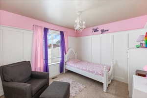 Bedroom featuring light colored carpet, a chandelier, and a decorative wall