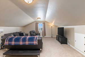 Bedroom featuring baseboards, light carpet, a textured ceiling, and vaulted ceiling