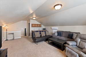 Living room with baseboards, an AC wall unit, vaulted ceiling, a textured ceiling, and light carpet