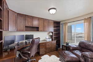 Office with dark wood-style flooring, built in desk, and a textured ceiling
