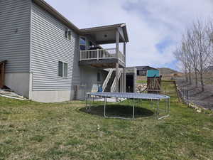 Rear view of property featuring a wooden deck, a yard, fence, a playground, and a trampoline