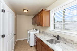 Clothes washing area featuring baseboards, cabinet space, a sink, a textured ceiling, and washing machine and dryer